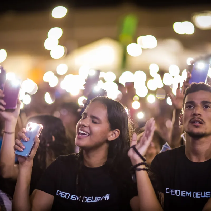 Multidão de jovens cantando com os celulares iluminados erguidos durante o Luau.