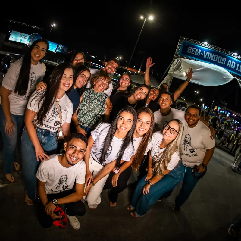 Grupo de jovens voluntários sorrindo diante do pórtico "Bem-vindos ao Luau com Cristo".